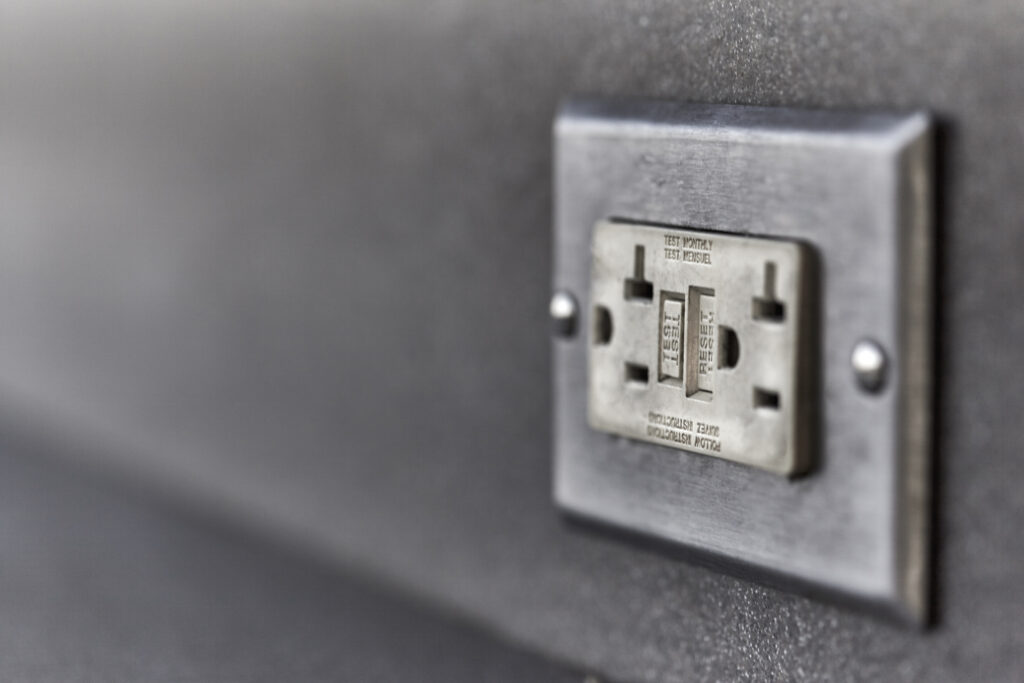 Close-up of a ground fault circuit interrupter electrical wall outlet on a gray wall.