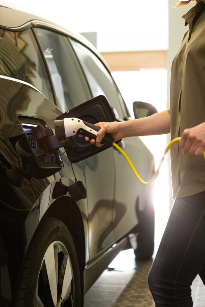 Woman plugs a charger into electric black car socket at home garage.