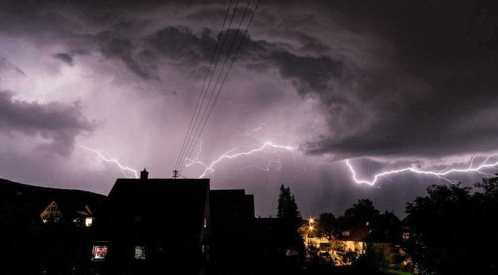 Neighborhood at night; lightning flashing in the background.